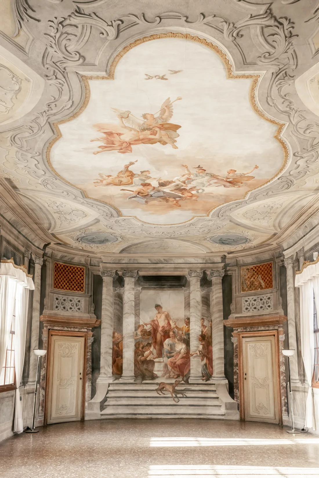 A frescoed ceiling with painted figures and stucco frames above a Venetian hall