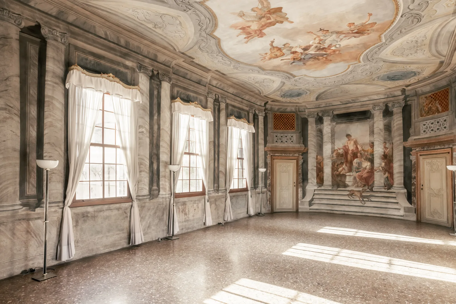 A bright Venetian hall with frescoed walls and ceiling, tall windows and a terrazzo floor