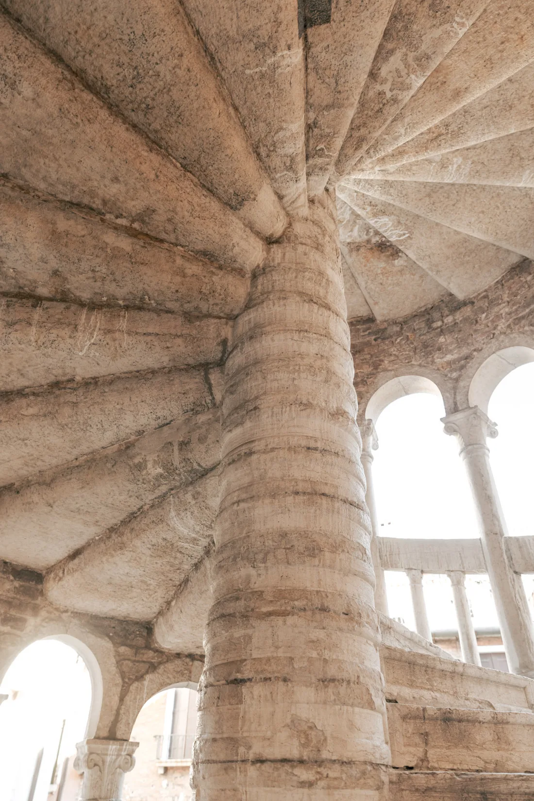 The stone steps of the staircase turning around the central column, lit through the arches