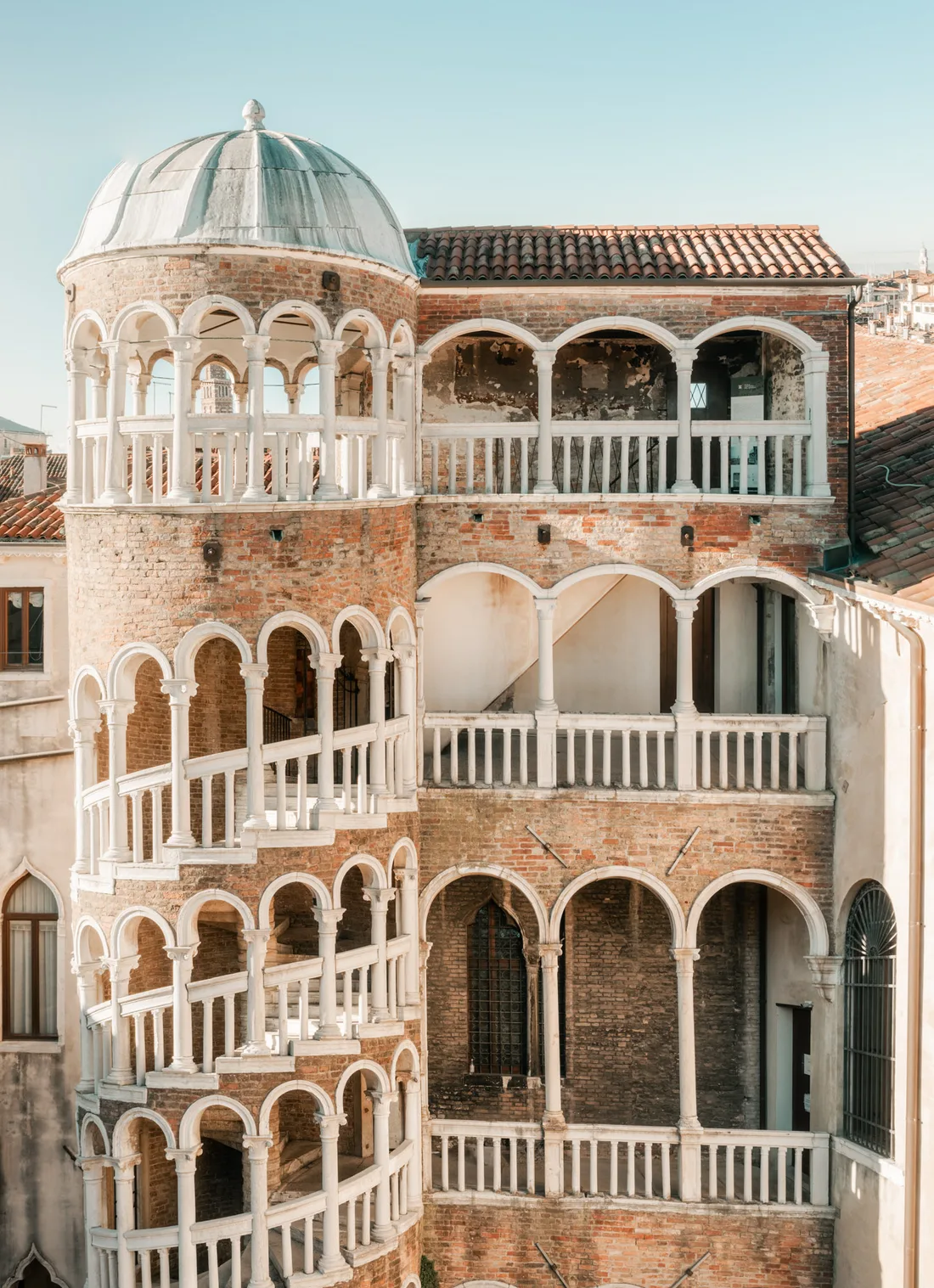 A Renaissance spiral staircase tower of white arches climbing the brick facade of a Venetian palace