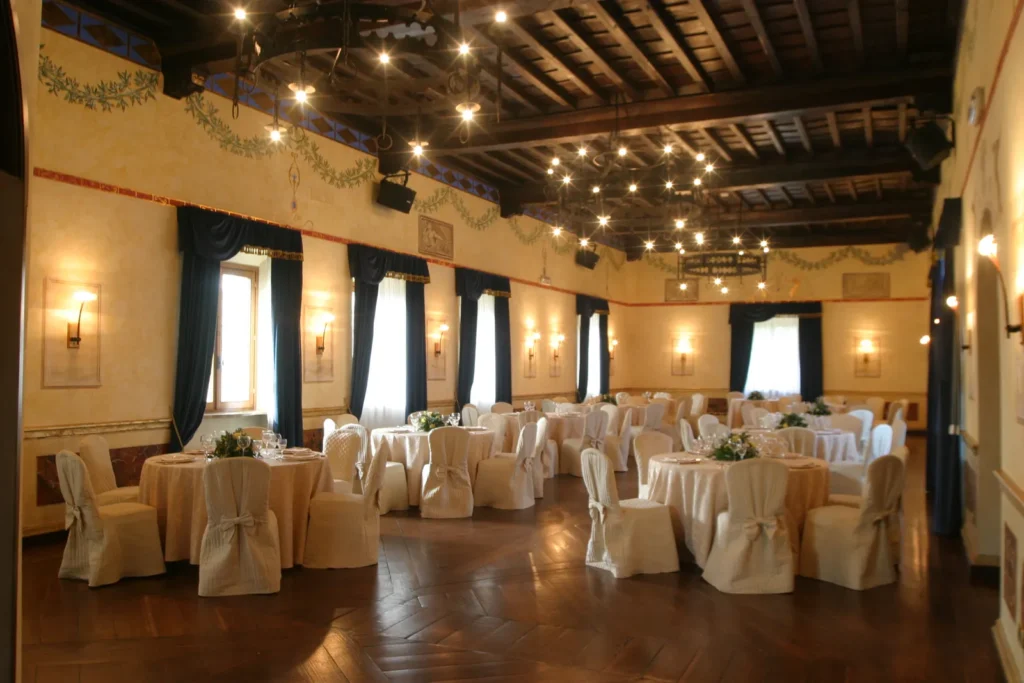 A grand banquet hall with a wooden beamed ceiling, round tables dressed in white and tall windows