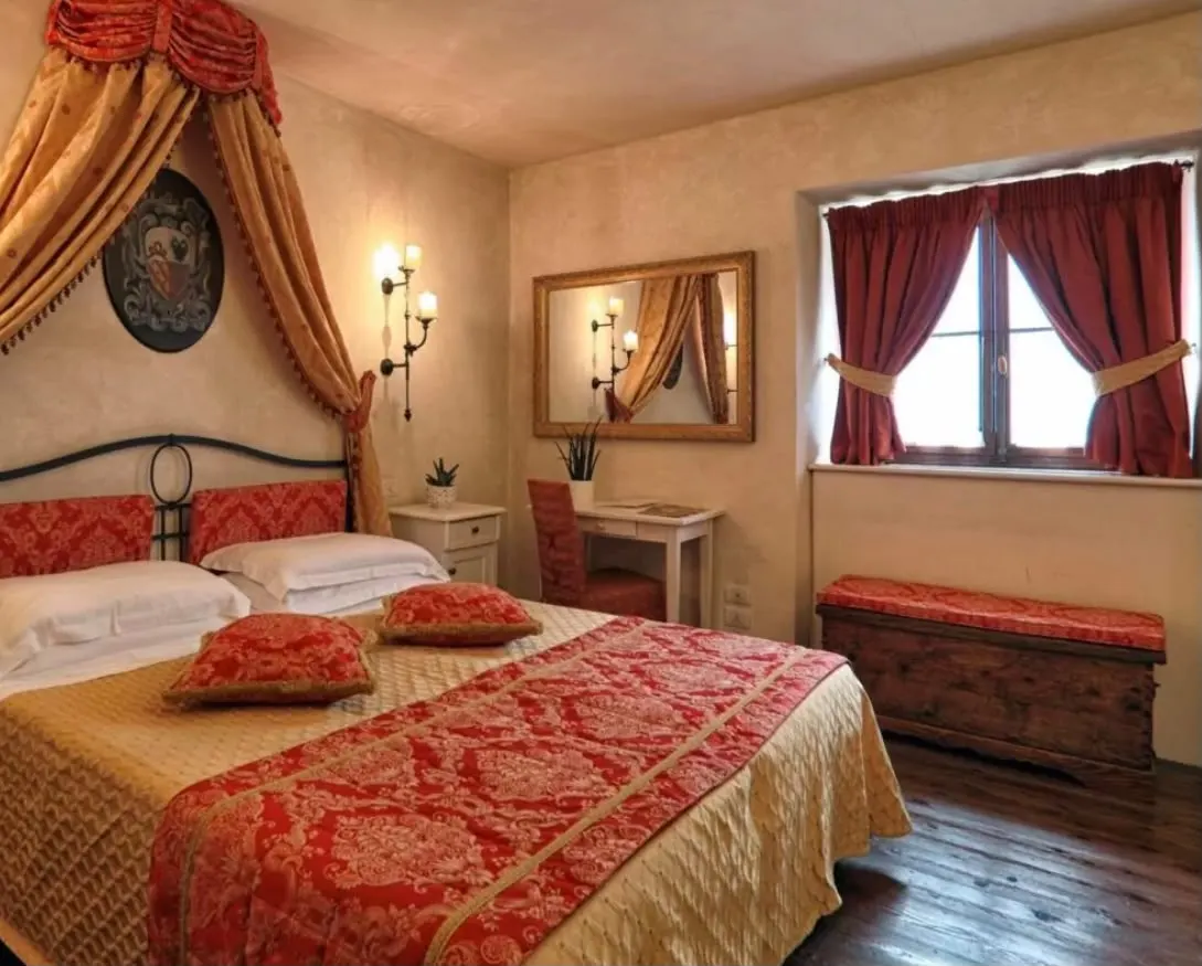 A classic double room in the castle with a canopy bed, red damask bedspread and wooden floor