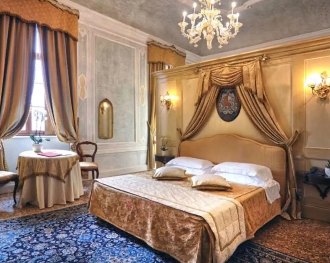 A junior suite in the castle with a draped canopy bed, a Venetian glass chandelier and a blue carpet