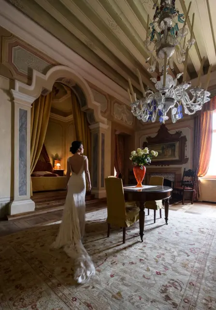A bride standing in a frescoed salon with a Venetian glass chandelier