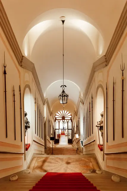 A long vaulted castle corridor with a red carpet leading to a ceremony room