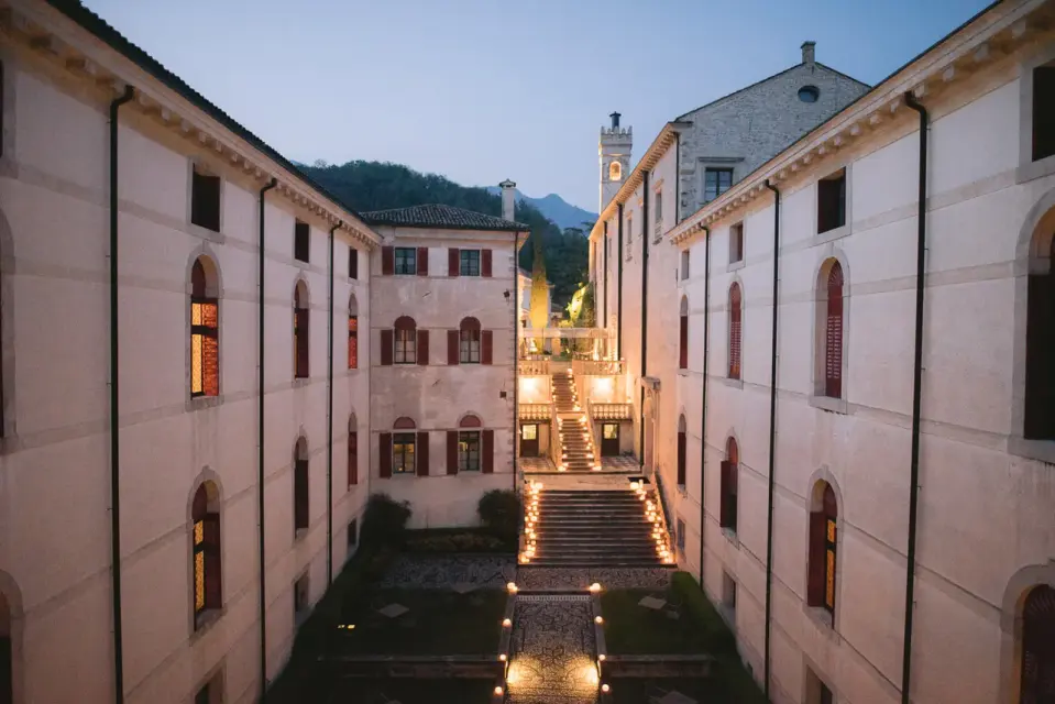 A castle courtyard at dusk, with lit windows and a stone staircase between two wings