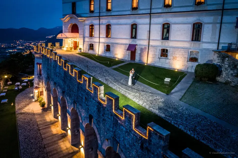 The illuminated castle walls and courtyard at night, with the lights of the valley below