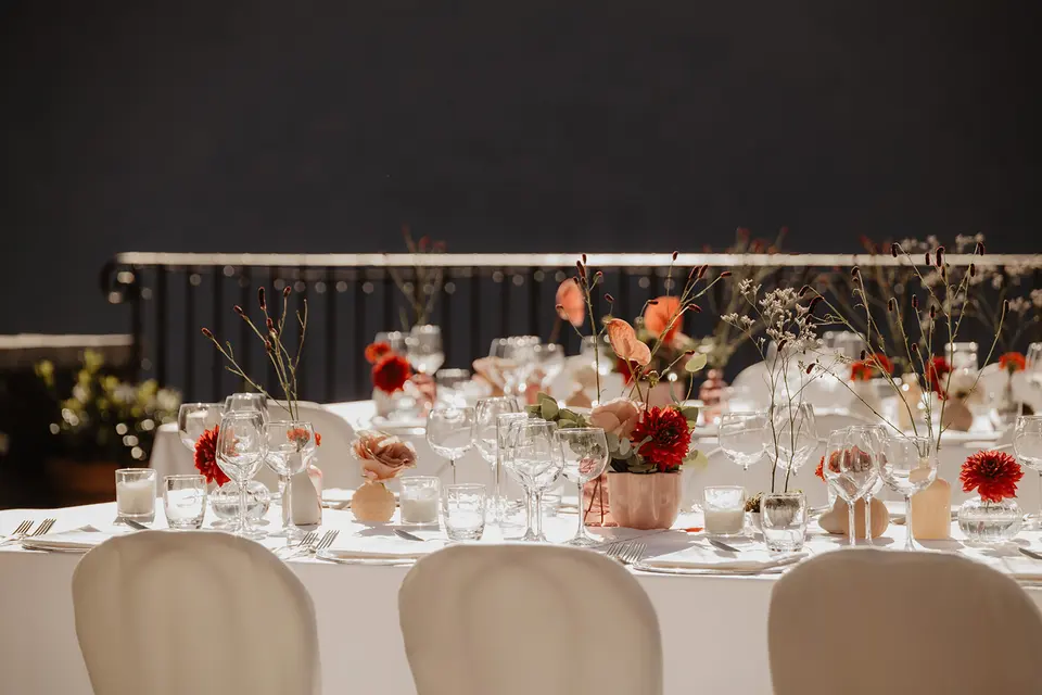 A wedding table set with glasses and red and orange flower arrangements