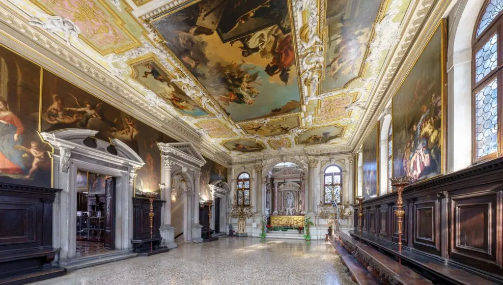 A long hall with a painted ceiling, carved wooden benches and an altar at the far end