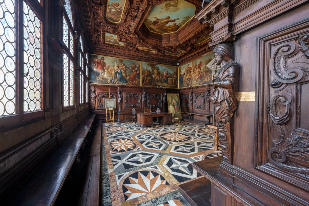 A hall with carved wooden panelling, painted ceiling and a marble inlaid floor