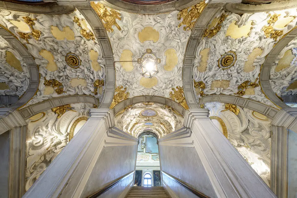 The grand staircase seen from below, under vaults covered in white and gold stucco
