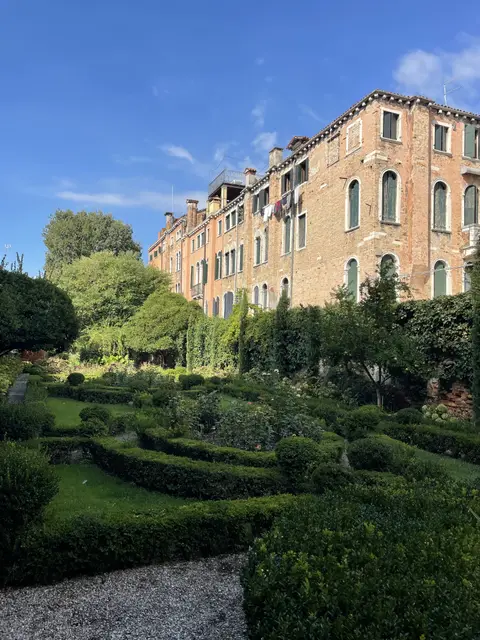 Clipped box hedges and flower beds in the palace garden, under a tall brick Venetian facade