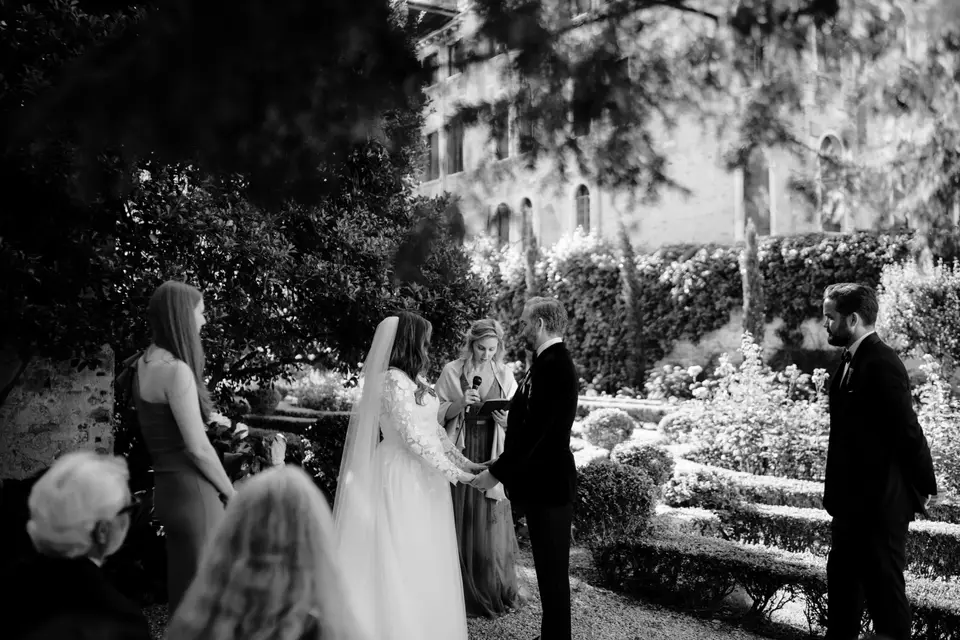 A black-and-white photo of a couple exchanging vows in the palace garden, surrounded by guests