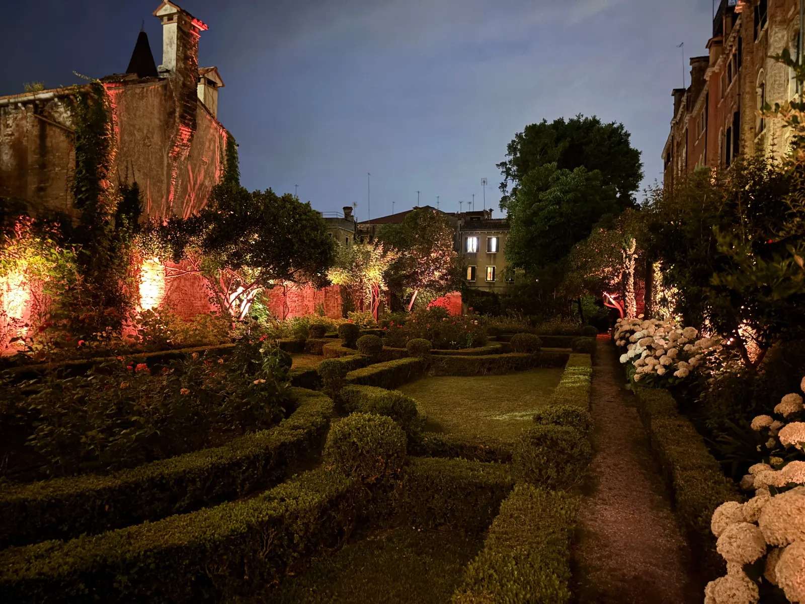 The Italian-style garden lit up in the evening, with box hedges, warm lights and hydrangeas