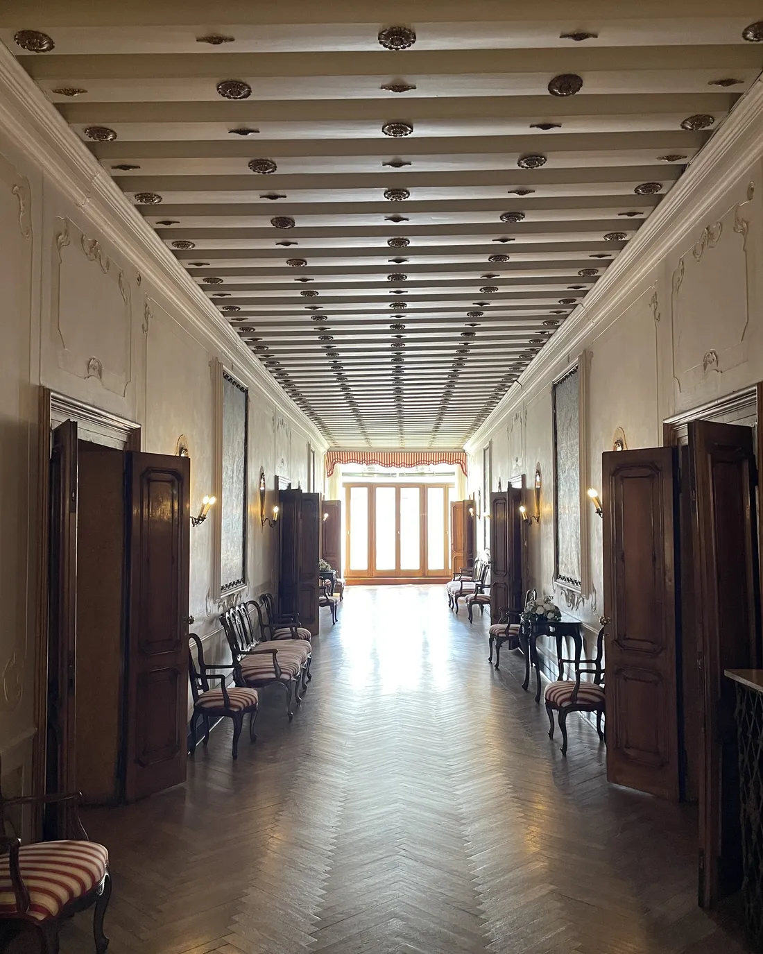 The long central hall of the noble floor, with a herringbone parquet floor and a coffered ceiling, leading to tall windows