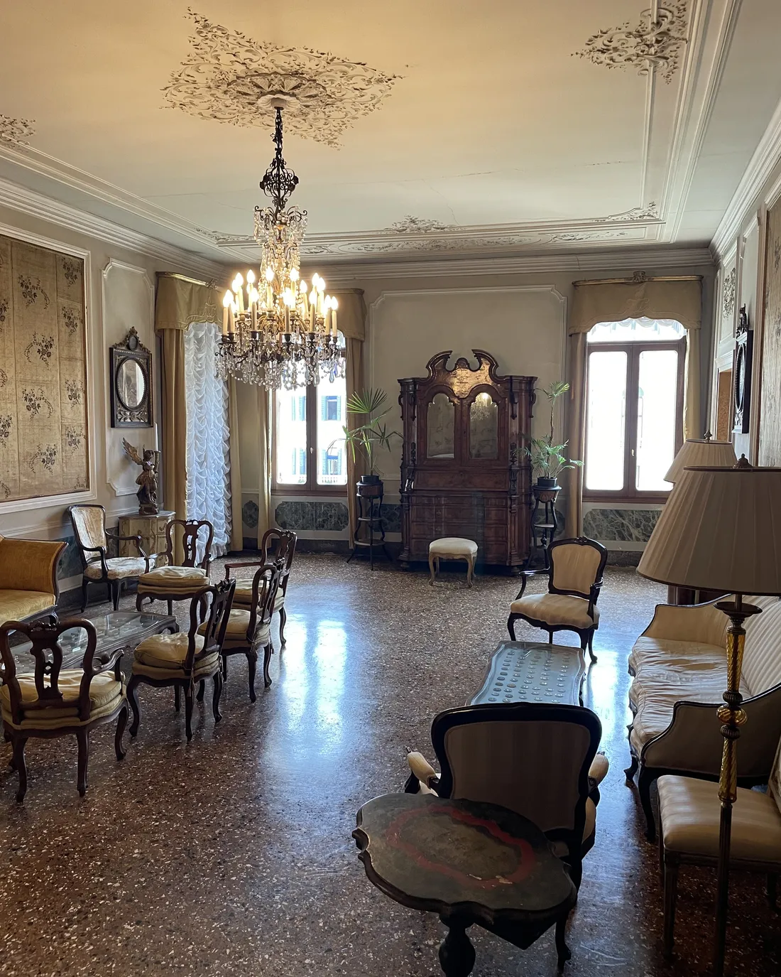 A side salon with a terrazzo floor, antique furniture, a tapestry and a glass chandelier