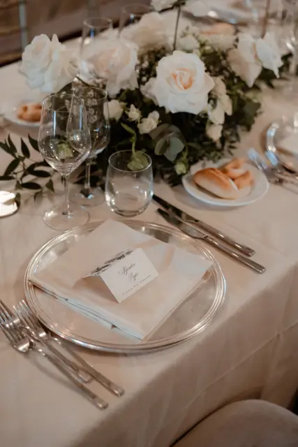 A wedding table setting with white roses, glasses and a place card