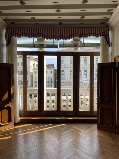 Tall windows with red curtains opening onto a balcony over the canal